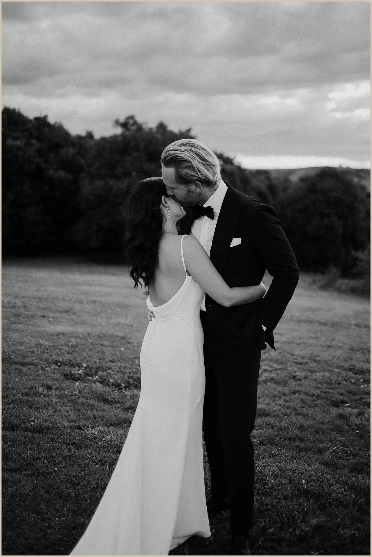 Jess & Rich at The Orchard Estate: The couple share a kiss in a paddock beneath a cloudy sky.