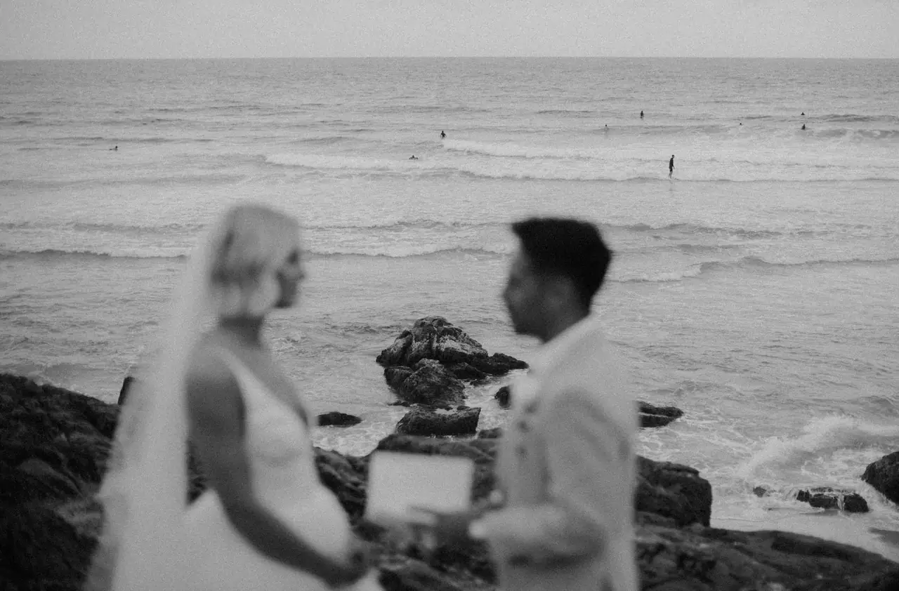 Black and white wedding portrait of a couple with the ocean behind them.