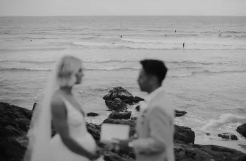 Black and white wedding portrait of a couple with the ocean behind them.
